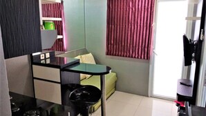 A compact living space with a kitchenette, a green sofa, a dining table, and a sliding door to the outside. - Green Pramuka Apartement By Vici (Jakarta)