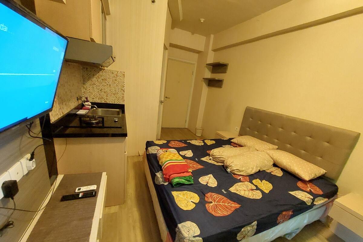 A bedroom with a bed, a television on a stand, a small desk, and a door.