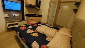A bedroom with a bed, a TV, a desk, and a wardrobe. - Green Pramuka Apartement By Vici (Jakarta)