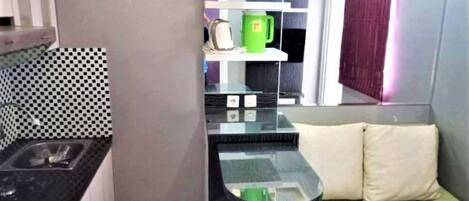 Cozinha compacta com bancada preta, uma pia e uma caneca verde em uma prateleira.