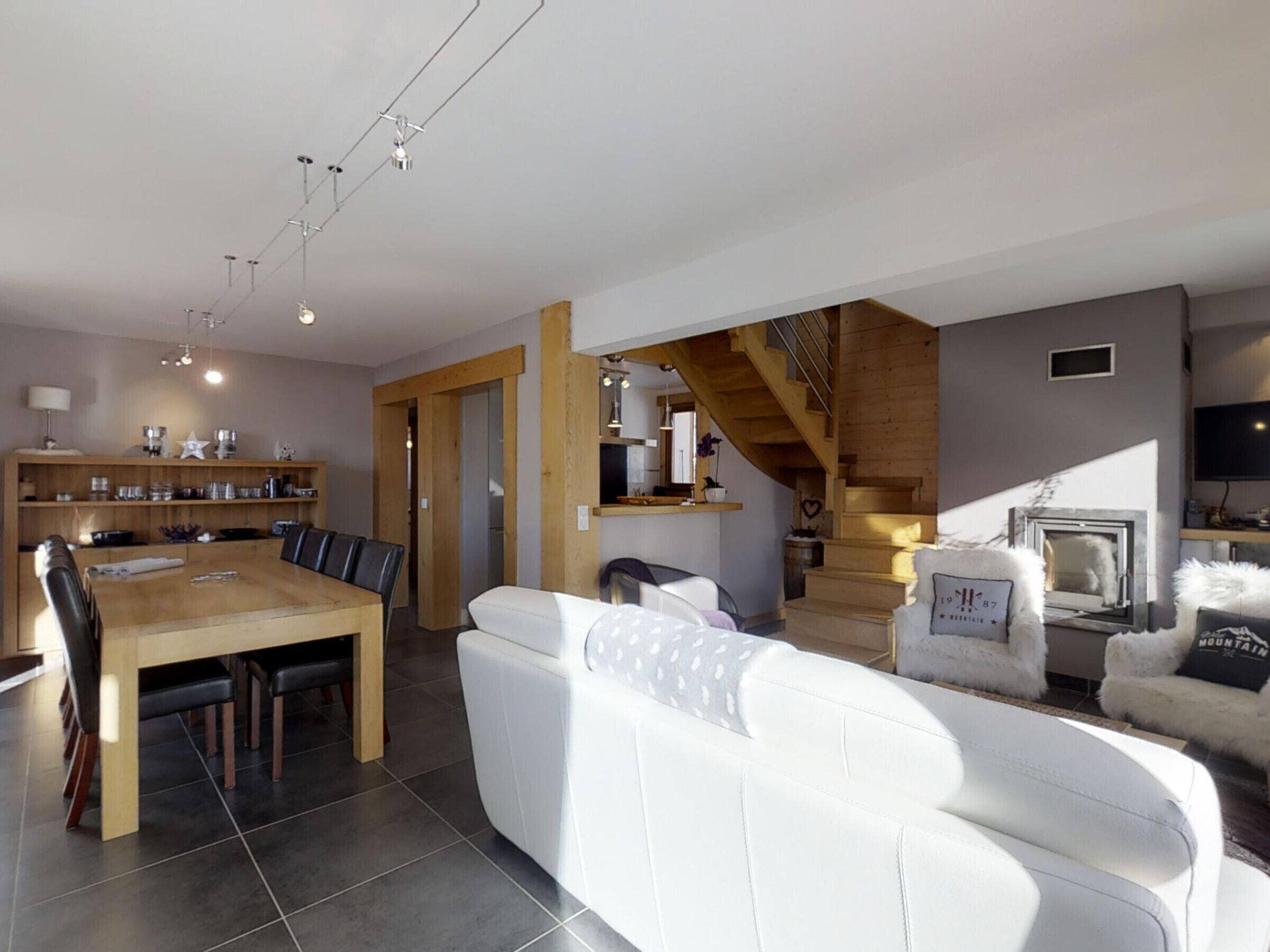 A spacious living area with a wooden dining table, white sofa, and a staircase leading to a loft.