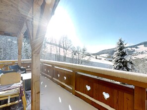 Un balcone in legno con vista su un paesaggio innevato e un cielo sereno.