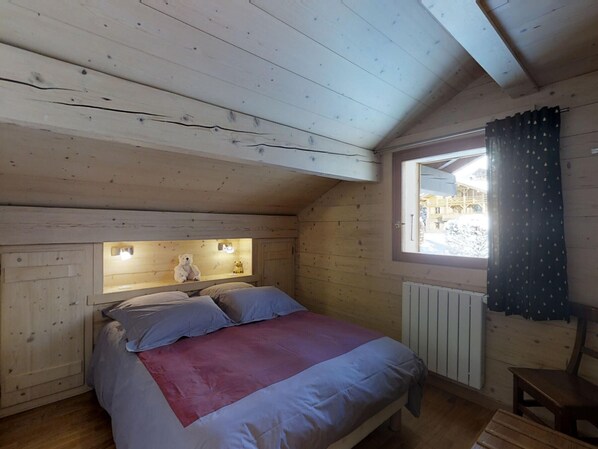 Una camera da letto accogliente in legno, con un letto, cuscini, un comodino e una finestra con tende.