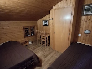 Une chambre dans un chalet en bois, avec deux lits, une petite table, une chaise et une armoire.