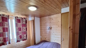 Una habitación con paneles de madera, una cama, una puerta y una ventana con cortinas.