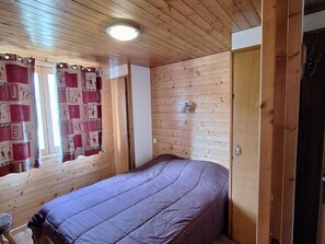 Une pièce aux murs lambrissés, avec un lit, une porte et une fenêtre ornée de rideaux.