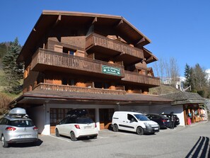 Un immeuble en bois à plusieurs étages, doté de balcons, avec une enseigne indiquant qu'il s'agit d'un immeuble d'appartements, et plusieurs voitures garées devant.