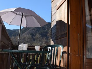 A wooden cabin with a balcony, a table with chairs, and a large umbrella.