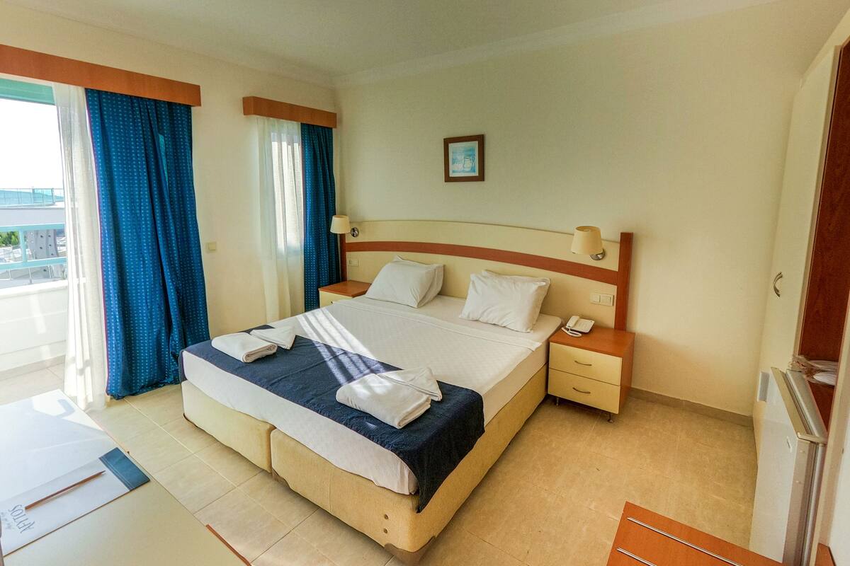 Habitación de hotel con una cama grande, dos mesitas de noche, un escritorio pequeño y vistas al exterior.