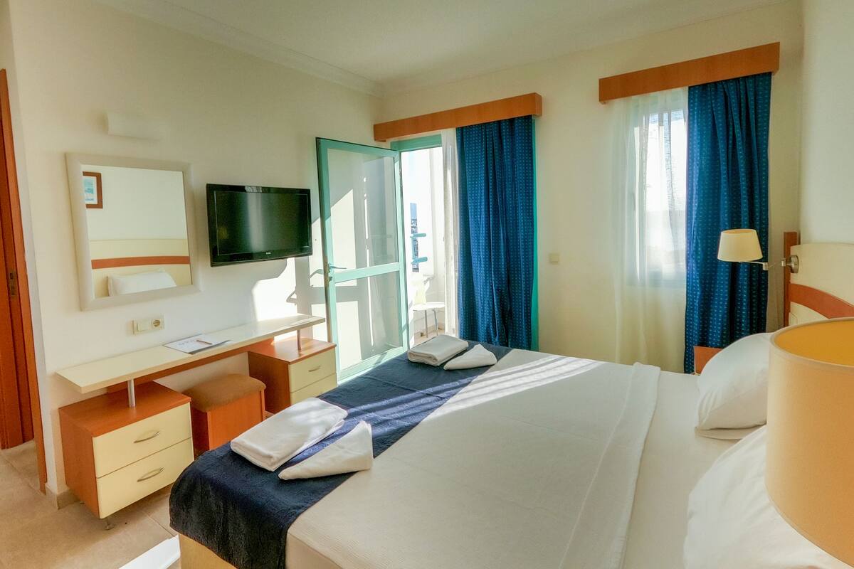 Habitación de hotel con cama, escritorio, televisor y ventana con cortinas.