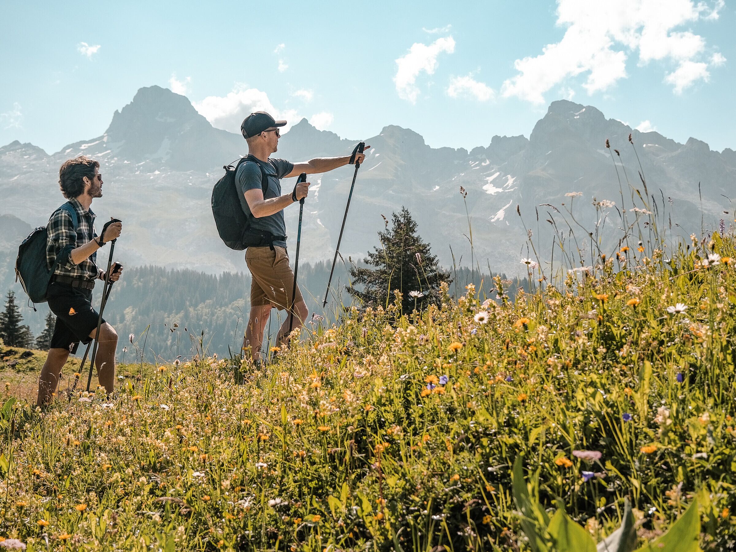 Two hikers on a mountain trail with a clear sky and distant mountains.