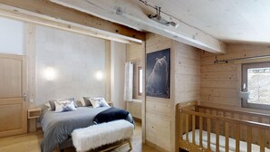 A wooden cabin interior with a bed, a crib, a bench, a radiator, and a bear painting. - Cozy apartment for 4 at the foot of the slopes (Le Grand-Bornand)