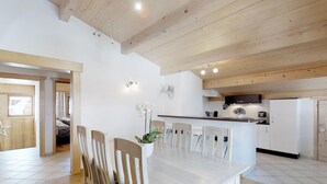 A modern kitchen with white cabinets, a central island, and a dining area with a wooden table and chairs. - Cozy apartment for 4 at the foot of the slopes (Le Grand-Bornand)
