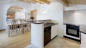 A modern kitchen with a dishwasher, sink, and oven. There is a dining area with wooden chairs and a table. - Cozy apartment for 4 at the foot of the slopes (Le Grand-Bornand)