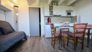 Um espaço de estar compacto com sofá, mesa de jantar com cadeiras, cozinha compacta e uma porta que dá para outro quarto.