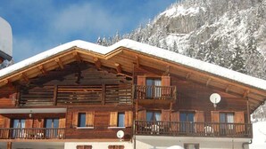 A wooden chalet with a balcony, surrounded by snow-covered mountains.