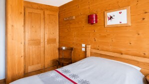 A wooden bedroom with a bed, a chair, a wardrobe, and a wall-mounted light fixture.