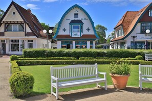 A cafe with a traditional European architectural style, a well-maintained garden with a bench, and a clear sky.