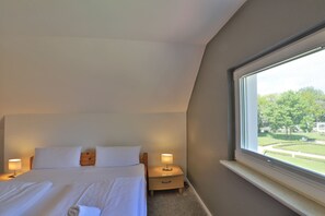 A hotel room with a bed, bedside lamps, a nightstand, and a window with a view of greenery.