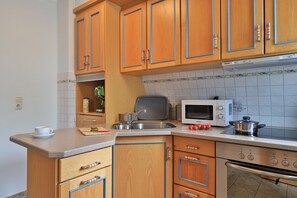 A compact kitchen with wooden cabinets, a microwave, a stove, and a coffee maker.