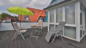 Une terrasse avec trois chaises longues, une table et un parasol vert.