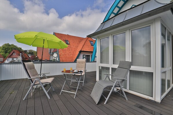 A deck with three lounge chairs, a table, and a green umbrella.