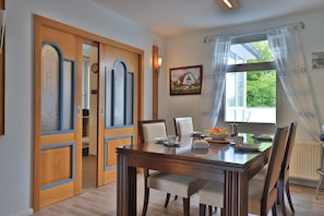 Un comedor con una mesa de madera, sillas y un ventanal con cortinas.