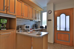 A compact kitchen with wooden cabinets, a microwave, a coffee maker, and a window with a clock.