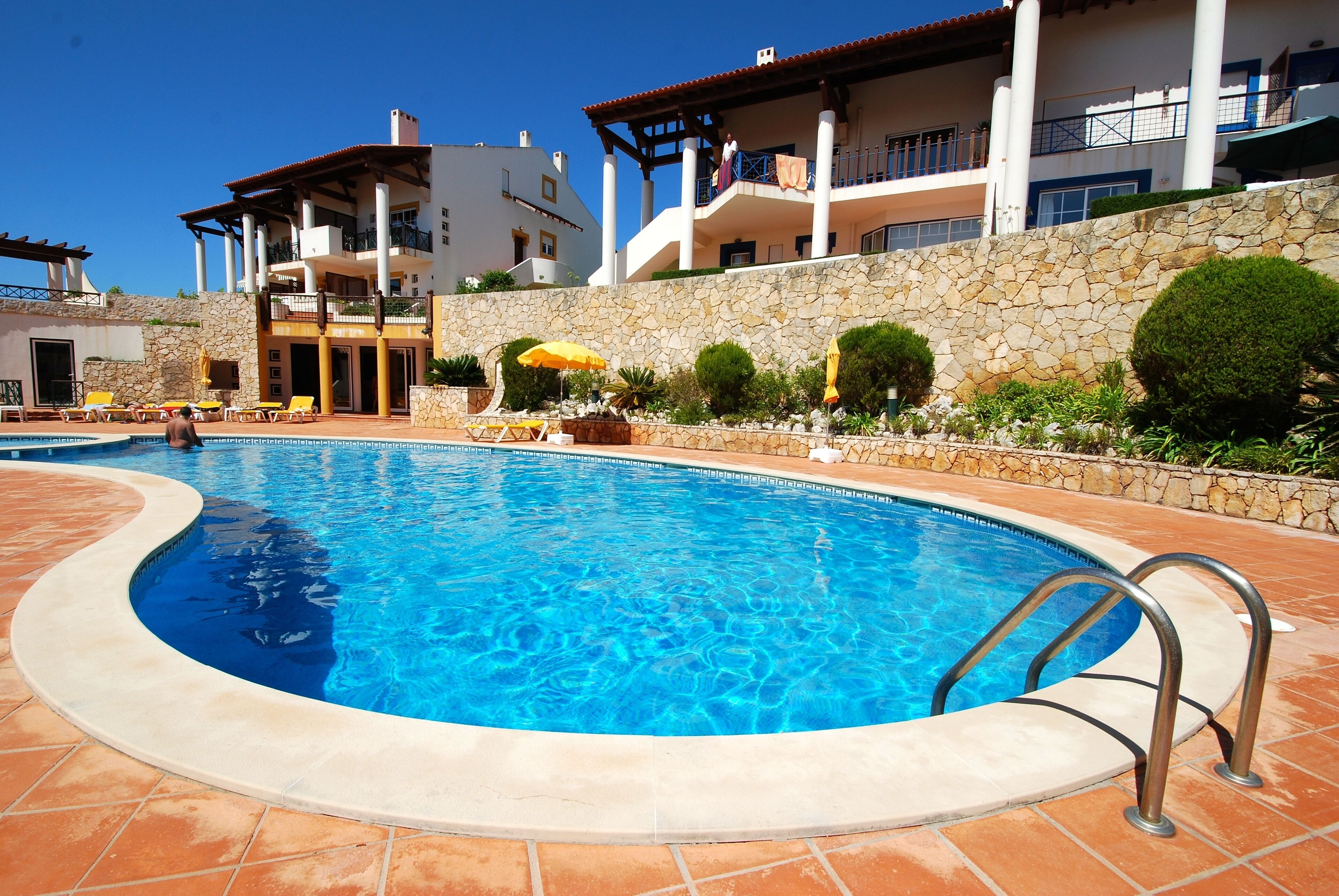A swimming pool with a stone wall and a tiled deck.