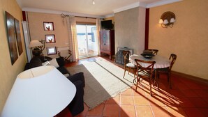 Een woonkamer met een bank, een eettafel met stoelen, een televisie op een kast en uitzicht door een glazen deur.