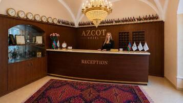 A reception desk with a chandelier, clocks, and flags.