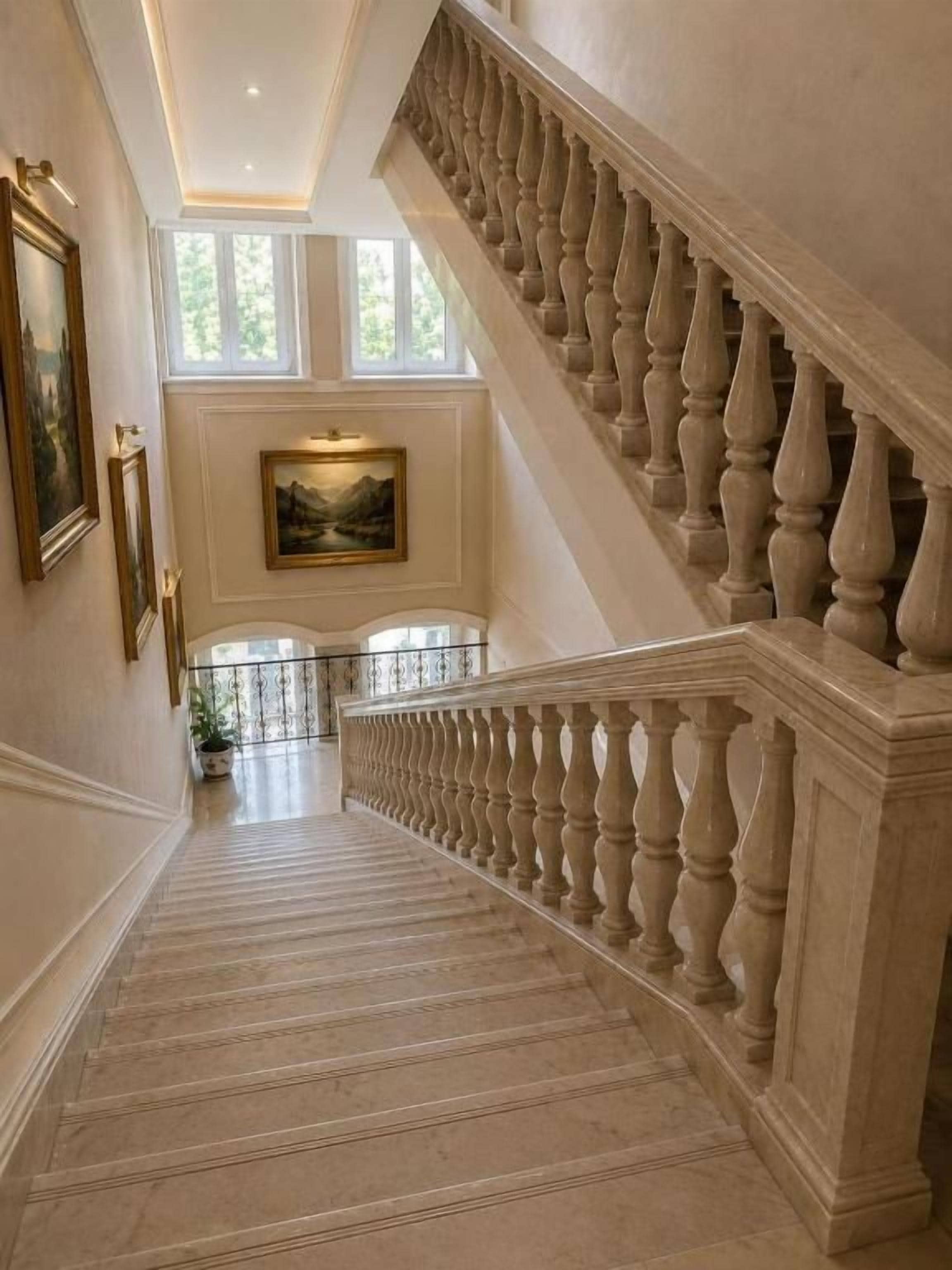 A grand staircase with balustrades leading to a landing with a painting and potted plants.