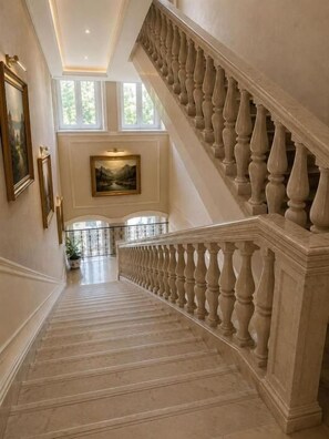 A grand staircase with balustrades leading to a landing with a painting and potted plants. - Azcot Center Hotel (Baku)