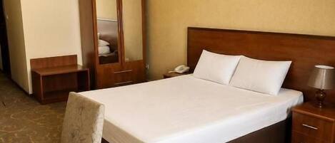 A hotel room with a large bed, a bedside table, a chair, a wardrobe, and a carpeted floor.