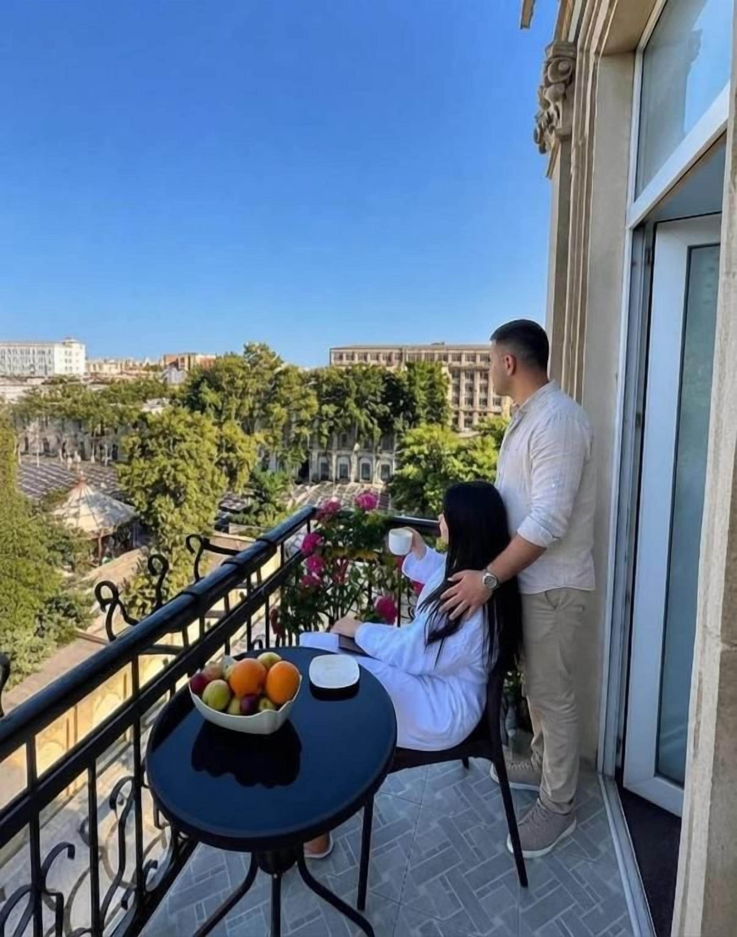 A balcony with a table, a bowl of fruit, and a person standing by the railing.