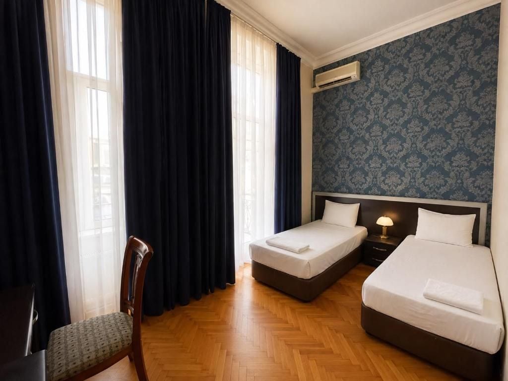 A hotel room with two single beds, a wooden chair, a desk, and a window with curtains.