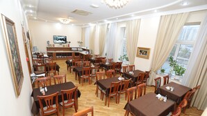 A dining area with multiple tables and chairs, a counter with a television, and a view of the outside through large windows. - Azcot Hotel - Nizami Street (Baku)