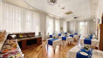 Een restaurantgedeelte van een hotel, met een buffet, gedekte tafels en een groot raam met gordijnen.
