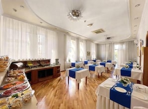 Une salle à manger d’hôtel avec un buffet, des tables dressées et une grande fenêtre avec des rideaux.
