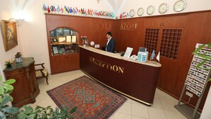 A reception area with a wooden reception desk, a clock, and a wall decorated with flags. - Azcot Hotel - Nizami Street (Baku)