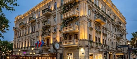 A multi-story hotel with balconies, a clock, and flags.