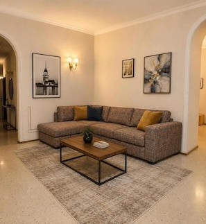 A living room with a sectional sofa, a coffee table, and framed artwork on the walls. - Azcot Center Hotel (Baku)
