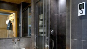 A modern bathroom with a glass-enclosed shower, a white sink, and a digital control panel.