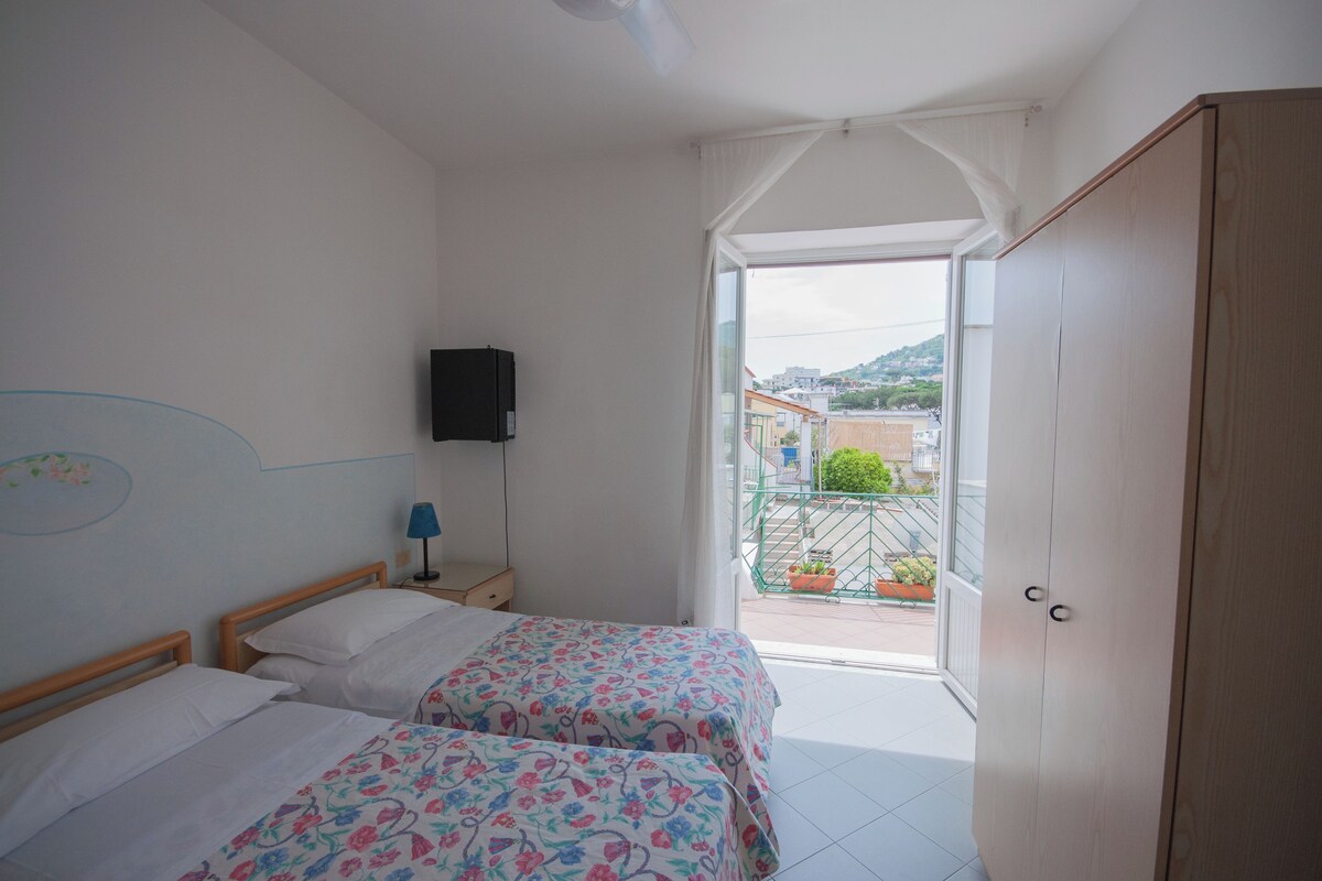 A bedroom with two beds, a television on the wall, and a view of the outside through a glass door.