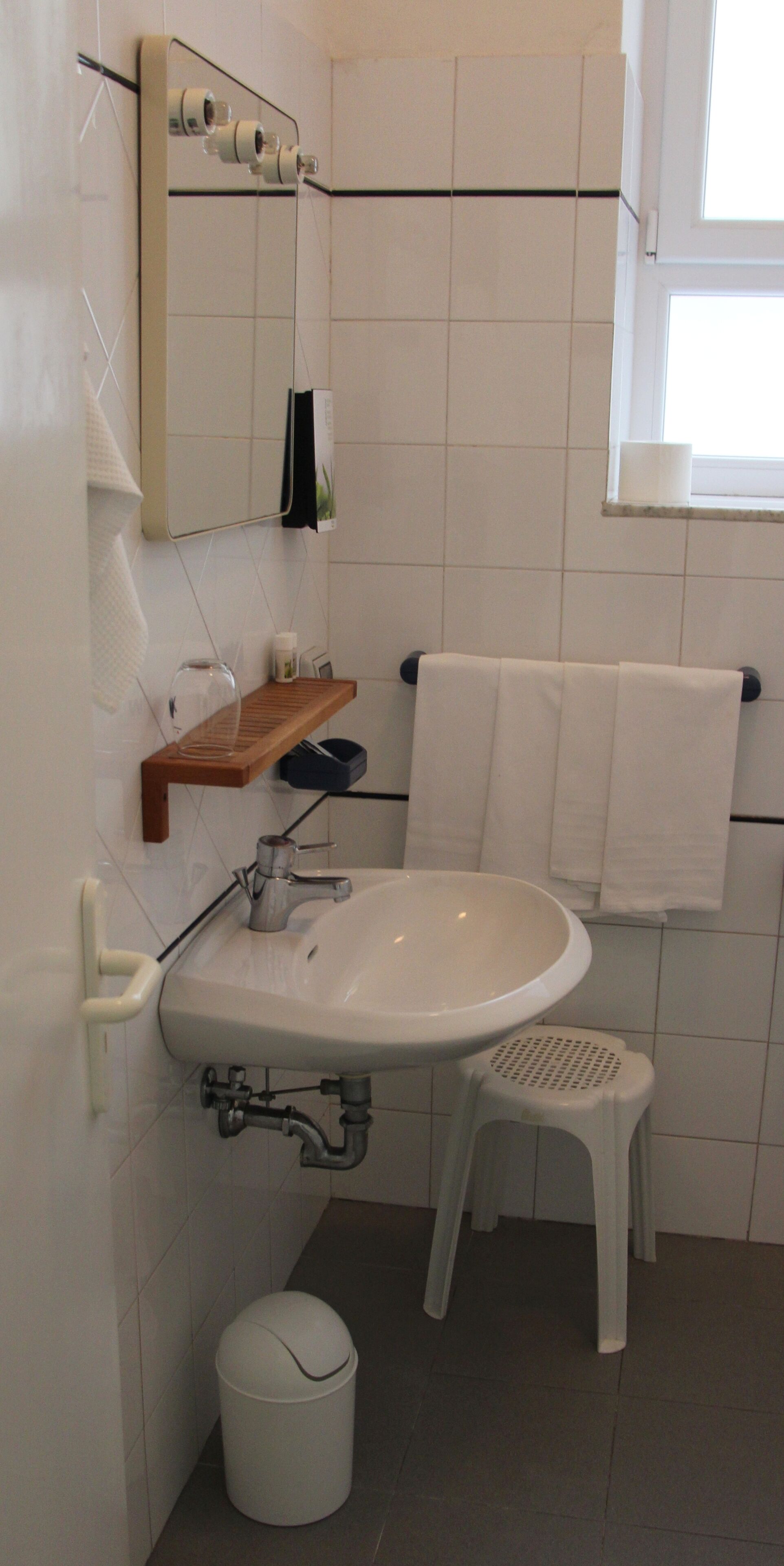 Un baño con lavamanos blanco, espejo y toallero.
