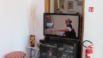 Una habitación con televisión, extintor, una pequeña mesa con una silla y un espejo en la pared.