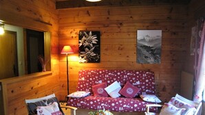 A cozy room with a wooden interior, a red floral sofa, two chairs, a table with a basket, a lamp, and a painting on the wall. - Spacious apartment for 6 in Le Grand-Bornand (Le Grand-Bornand)