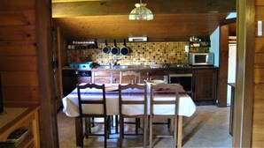 A wooden interior with a dining table set for four, a kitchen with a tiled backsplash, and a hanging light fixture. - Spacious apartment for 6 in Le Grand-Bornand (Le Grand-Bornand)
