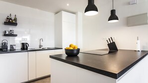 A modern kitchen with white cabinetry, a black countertop, and a bowl of lemons. There are black pendant lights, a knife block, and a coffee maker on the counter. - SW Bailen Beautiful views (Málaga)