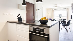 A modern kitchen with a central island, black pendant lights, and a dining area with a table and chairs. - SW Bailen Beautiful views (Málaga)